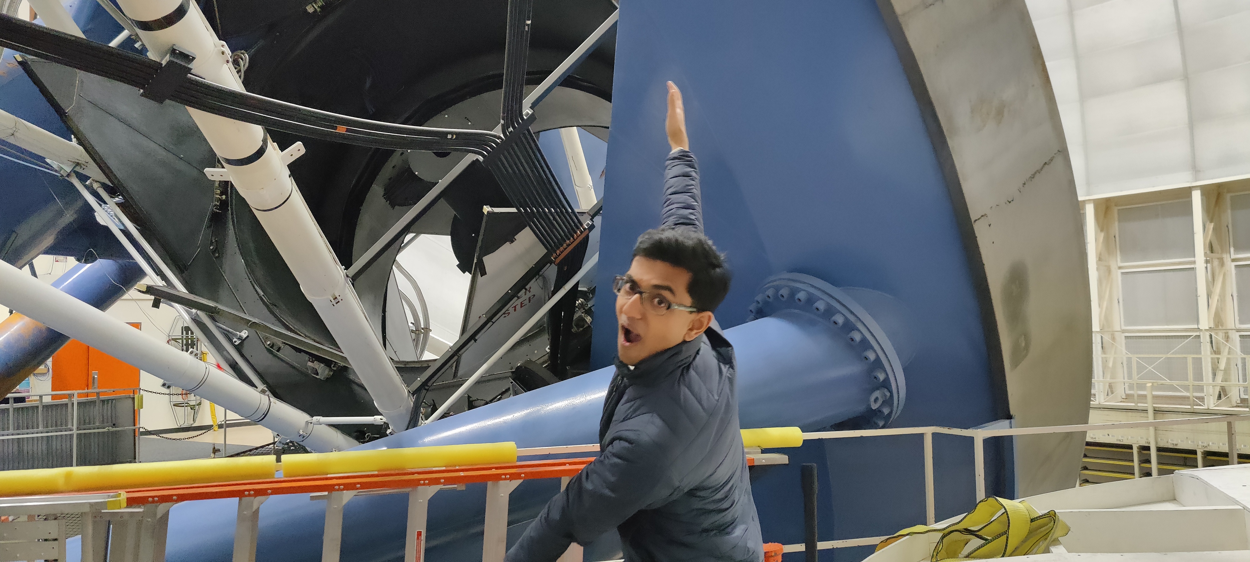 Me posing in front of the Dark Energy Spectroscopic Instrument, mounted on the Mayall Telescope on Kitt Peak, Arizona.